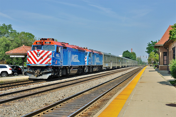 The FRA released 25 million additional dollars in federal grant money to assist local communities to enhance grade crossing safety. Here, a Chicago Metra commuter train speeds over a busy road crossing in west suburban Hinsdale, Illinois on a sunny afternoon in August of 2014. Image © 8/2014 by Nikki Burgess; all rights reserved.